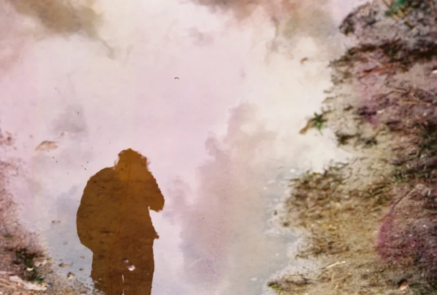 Man reflected in a purple-ish puddle.