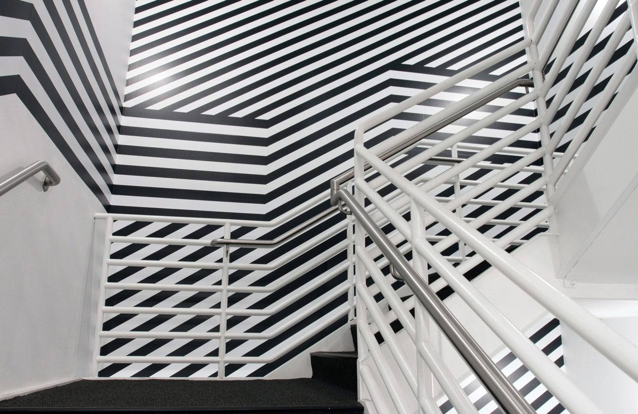 White railing along a staircase contrasts with a bold black and white striped design, creating an almost psychedelic visual effect.